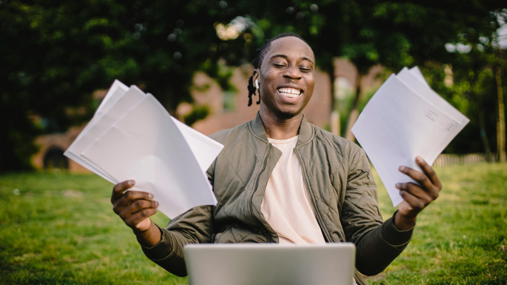Man laughing and smiling holding pages in front of a laptop