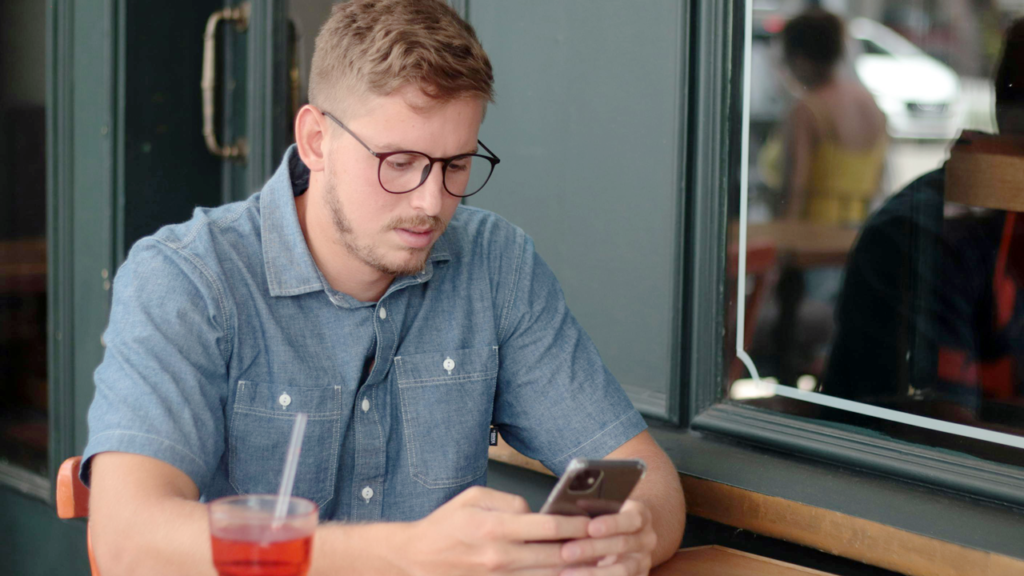 guy sitting outside restaurant looking at smart phone