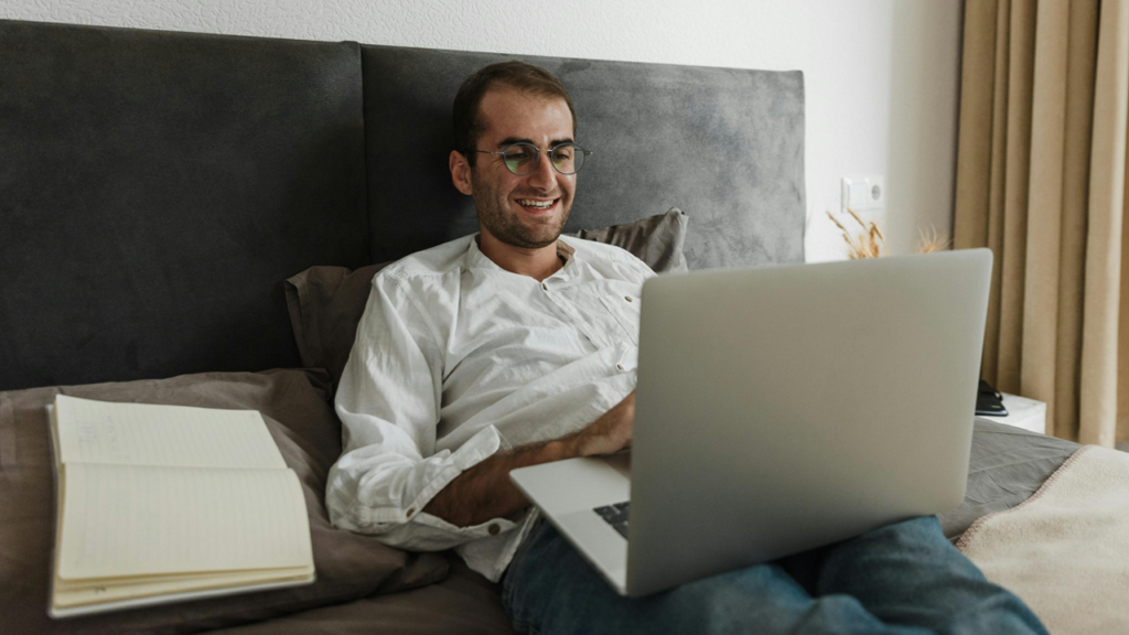 Guy sitting on bed worrking on a laptop