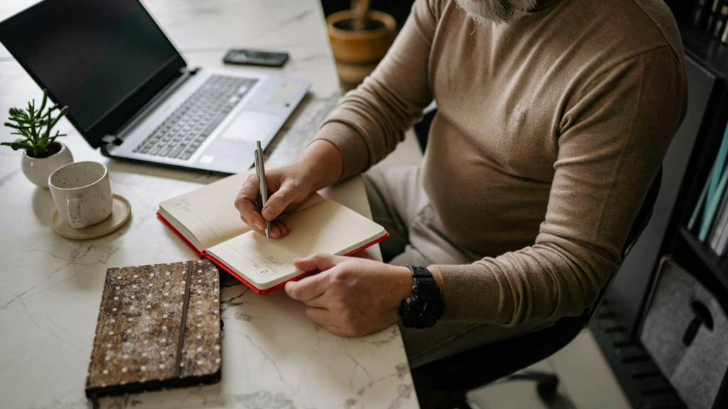 Elder man writing in a journal away from a laptop