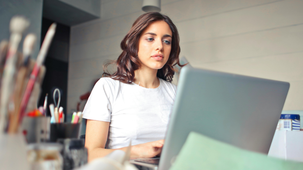 Woman working on a laptop next to art supplies